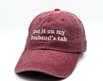 May include: A maroon baseball cap with the text "put it on my husband's tab" embroidered in white.