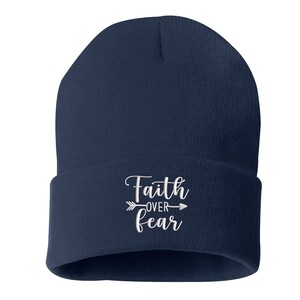 K&ouml;nnte beinhalten: Eine marineblaue Beanie-M&uuml;tze mit dem gestickten Schriftzug "Faith over Fear" in Wei&szlig;. Der Text wird von einem Pfeildesign begleitet. Die M&uuml;tze ist ein einfacher, klassischer Stil.