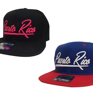 May include: Two baseball caps with the text "Puerto Rico" in a cursive script. One cap is black with pink lettering and the other is blue with white lettering. Both caps have a red brim.