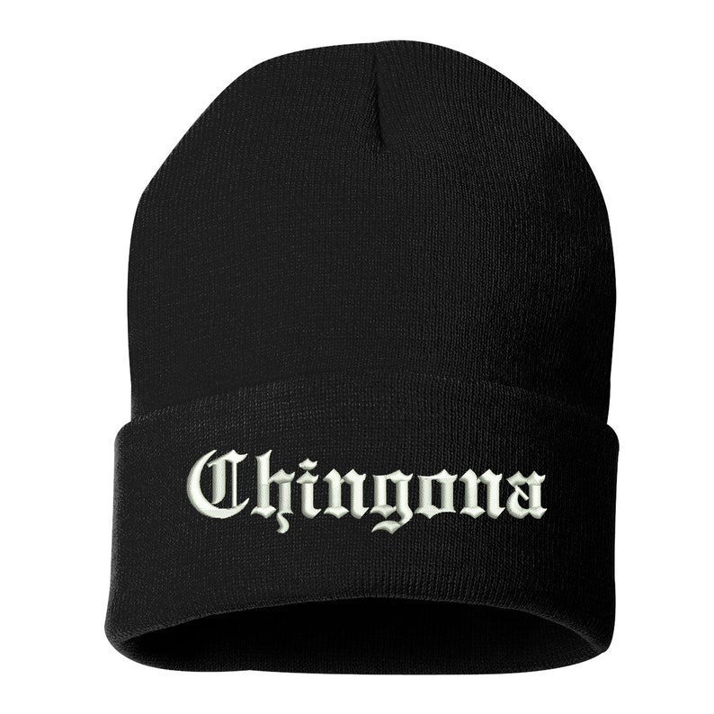 May include: Black beanie hat with the word "Chingona" embroidered in white, gothic-style lettering across the folded brim. The hat is made of a soft, knitted material.
