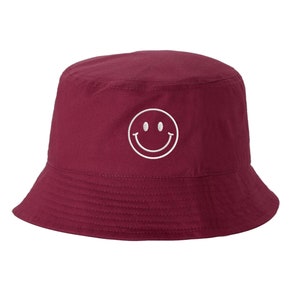 May include: A burgundy bucket hat with a white embroidered smiley face.