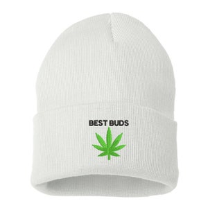 May include: White beanie with the embroidered text "BEST BUDS" above a green cannabis leaf. The beanie is made of a soft, knitted material and has a folded cuff.