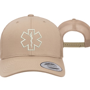May include: A tan trucker hat with a white embroidered medical symbol, the Star of Life, with a snake and staff. The hat has a mesh back and a snap closure. The hat is made by The Classic Snapback.