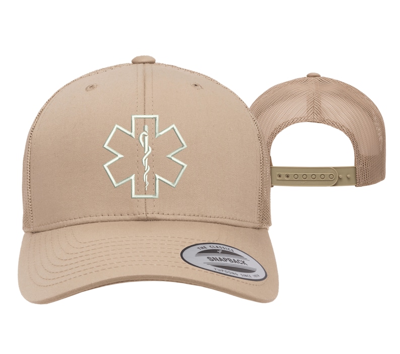 May include: A tan trucker hat with a white embroidered medical symbol, the Star of Life, with a snake and staff. The hat has a mesh back and a snap closure. The hat is made by The Classic Snapback.