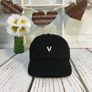 May include: Black baseball cap with a white letter V embroidered on the front.
