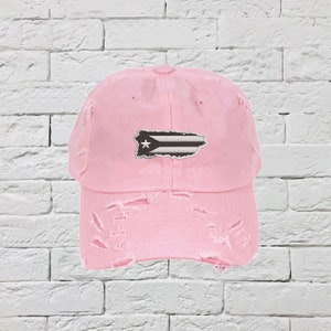 May include: A pink distressed baseball cap with a white star and black and white Puerto Rican flag patch.