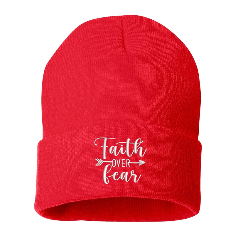 K&ouml;nnte beinhalten: Eine leuchtend rote Beanie-M&uuml;tze mit umgeschlagenem Saum. Auf der M&uuml;tze ist der gestickte Schriftzug "Faith over Fear" in wei&szlig;er Schrift mit einem Pfeildesign zu sehen. Die Beanie besteht aus weichem Strickmaterial.