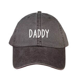 May include: A black, adjustable, cotton baseball cap with the word "DADDY" embroidered in white on the front.