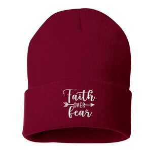 K&ouml;nnte beinhalten: Burgunderfarbene Beanie-M&uuml;tze mit umgeschlagenem Saum. Der wei&szlig;e, gestickte Text "Faith over Fear" ist mittig auf der Vorderseite angebracht, mit einem Pfeildesign. Die M&uuml;tze ist aus weichem Strickmaterial.