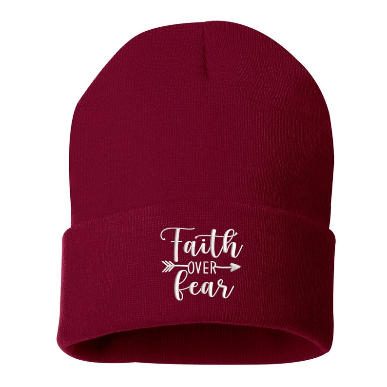 K&ouml;nnte beinhalten: Burgunderfarbene Beanie-M&uuml;tze mit umgeschlagenem Saum. Der wei&szlig;e, gestickte Text "Faith over Fear" ist mittig auf der Vorderseite angebracht, mit einem Pfeildesign. Die M&uuml;tze ist aus weichem Strickmaterial.