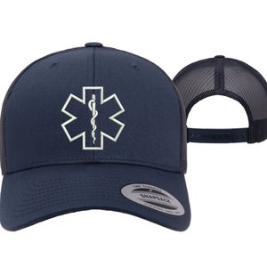 May include: A navy blue trucker hat with a white embroidered medical symbol, the Star of Life, on the front. The hat has a black mesh back and a snap closure.