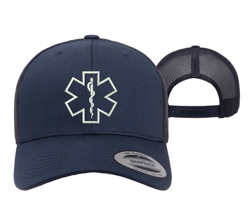 May include: A navy blue trucker hat with a white embroidered medical symbol, the Star of Life, on the front. The hat has a black mesh back and a snap closure.