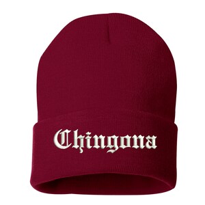 May include: A burgundy beanie with the word "Chingona" embroidered in white, gothic-style lettering across the folded brim. The hat is made of a soft, knitted material.