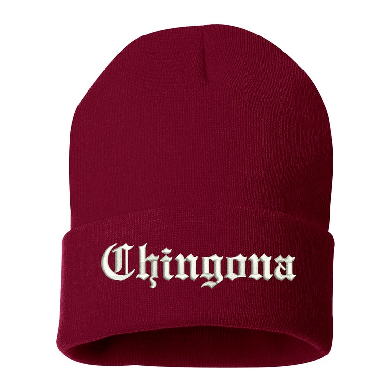 May include: A burgundy beanie with the word "Chingona" embroidered in white, gothic-style lettering across the folded brim. The hat is made of a soft, knitted material.