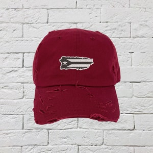 May include: A maroon distressed baseball cap with a white and black embroidered Puerto Rican flag.
