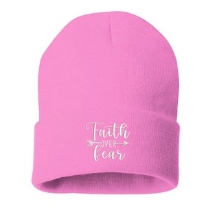 K&ouml;nnte beinhalten: Ein hellrosa Beanie mit dem wei&szlig;en Schriftzug "Faith Over Fear" und einem Pfeildesign. Der Beanie besteht aus einem weichen, gestrickten Material, ideal f&uuml;r kaltes Wetter.