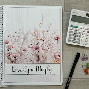 May include: A white spiral bound notebook with a floral design and the name "Brooklynn Murphy" printed on the cover.