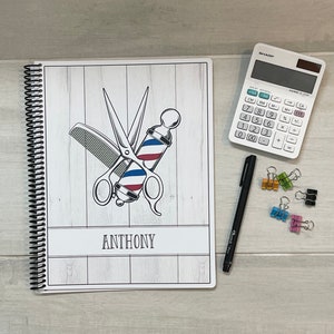 May include: A white spiral bound notebook with a wood grain background. The notebook has a barber pole and scissors design with the name "ANTHONY" printed below the design.