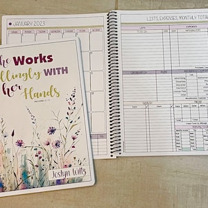 May include: A white planner with a floral design and the text "She Works Willingly With Her Hands" and "Proverbs 31:13". The planner has a white spiral binding and the name "Joslyn Willz" is printed on the cover.