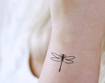 May include: A woman with blonde hair has a small dragonfly tattoo on her wrist.