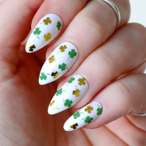 May include: White stiletto nails with gold and green shamrock decals.