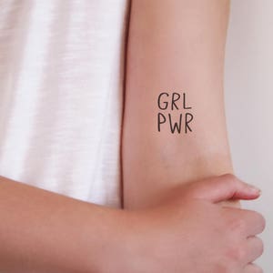 May include: A temporary tattoo with the text "GRL PWR" on a person's arm.