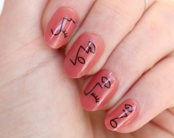 May include: Close-up of a hand with five nails painted a light peach color. Each nail has a simple black line drawing of a face with eyes, nose, and mouth.