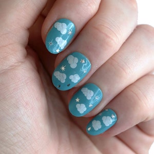 May include: Close-up of a hand with blue nail polish featuring white clouds and silver glitter accents.