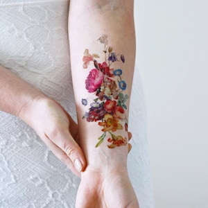 Puede incluir: Un tatuaje temporal que presenta un ramo de flores coloridas en un estilo vintage. El tatuaje se aplica en el brazo de una persona.