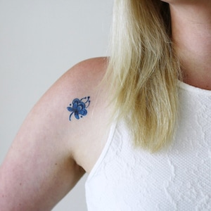May include: A small blue flower tattoo on a person's shoulder.