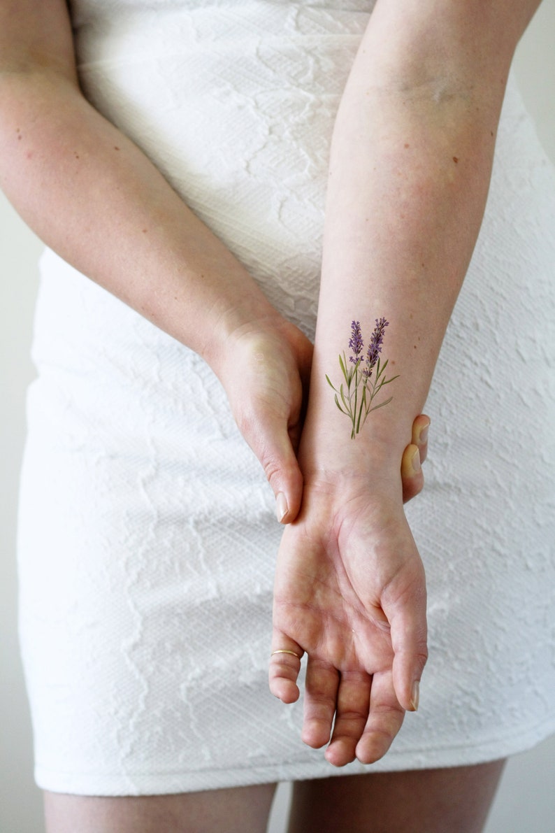 May include: A close-up of a person's wrist with a small lavender flower tattoo.