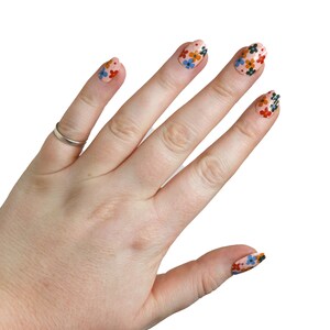 K&ouml;nnte beinhalten: Eine Hand mit rosafarbenem Nagellack und Blumenmustern auf den N&auml;geln. Die N&auml;gel sind oval geformt und die Blumen sind rot, orange, blau und gr&uuml;n.