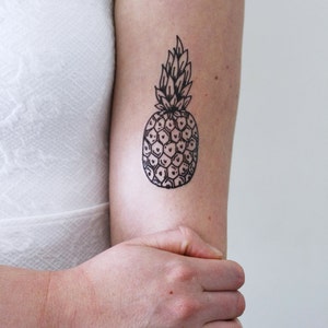 May include: A black and white line drawing of a pineapple on a person's arm.