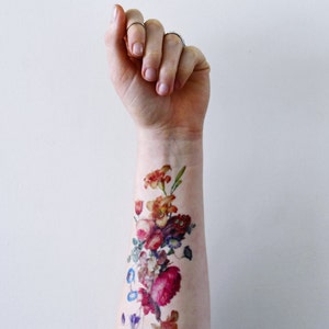May include: A colorful floral tattoo on a person's arm. The tattoo features a variety of flowers in shades of red, pink, orange, yellow, and blue.