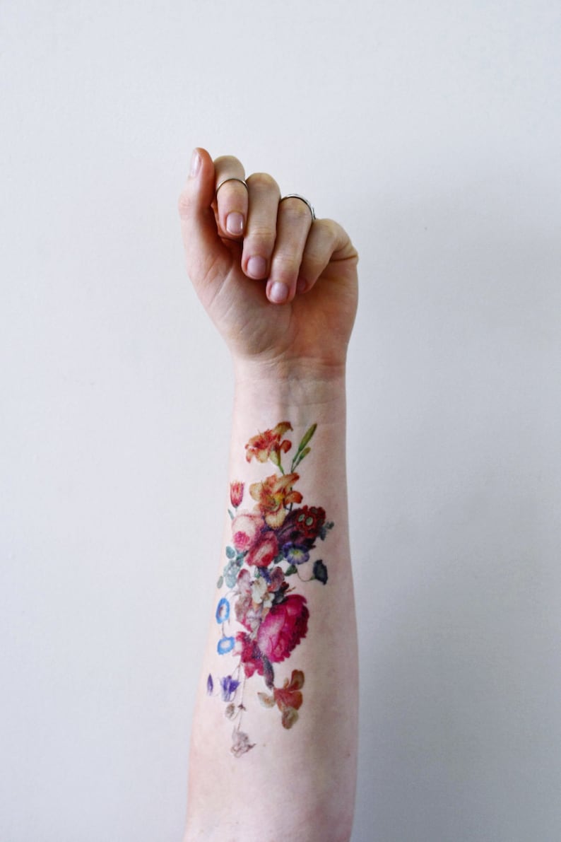 May include: A colorful floral tattoo on a person's arm. The tattoo features a variety of flowers in shades of red, pink, orange, yellow, and blue.