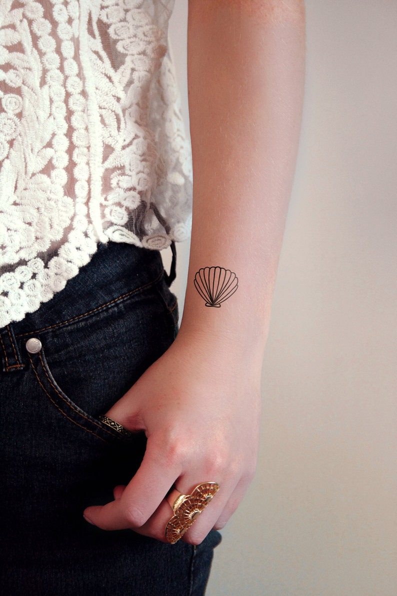 May include: A simple black line drawing of a seashell on a person's wrist.