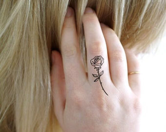 Könnte beinhalten: Eine einfache Linienzeichnung einer Rose mit Stiel und Blättern ist auf den Finger einer Person tätowiert.