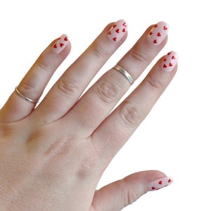 May include: A hand with pink nail polish with red heart designs on each finger.