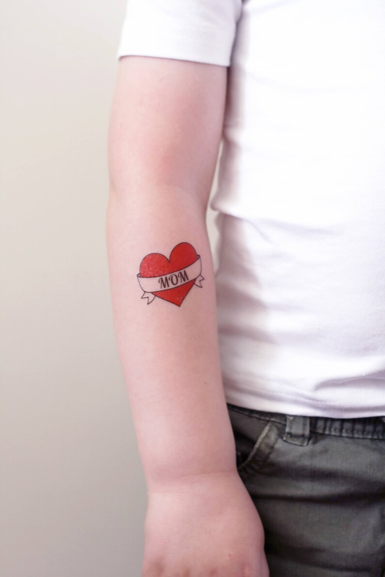May include: A red heart with a white banner that says "MOM" on it. The heart is a temporary tattoo.