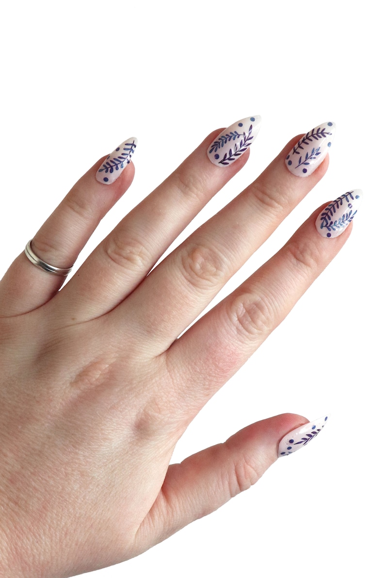 May include: A hand with white nail tips with a blue floral design. The nails are long and pointed.