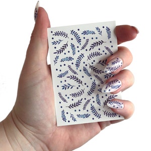 May include: A sheet of nail art stickers with a white background and a pattern of blue and purple leaves and dots.