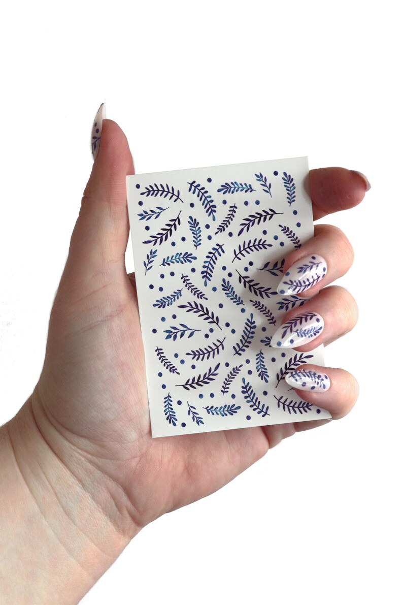 May include: A sheet of nail art stickers with a white background and a pattern of blue and purple leaves and dots.