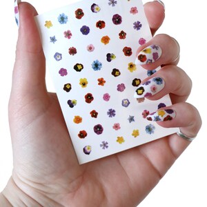 May include: A sheet of nail stickers with small, colorful flower designs. The sheet is white and has a variety of flower colors, including purple, pink, yellow, and blue.