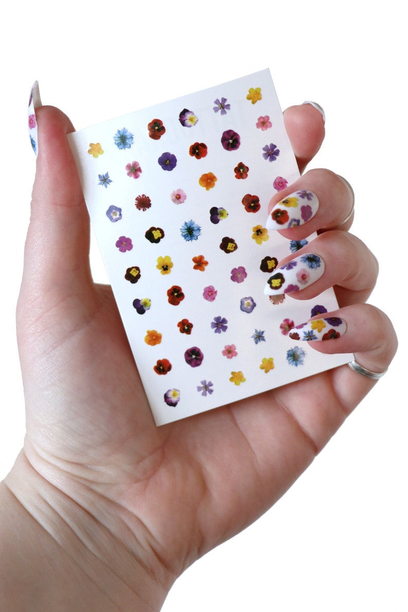 May include: A sheet of nail stickers with small, colorful flower designs. The sheet is white and has a variety of flower colors, including purple, pink, yellow, and blue.
