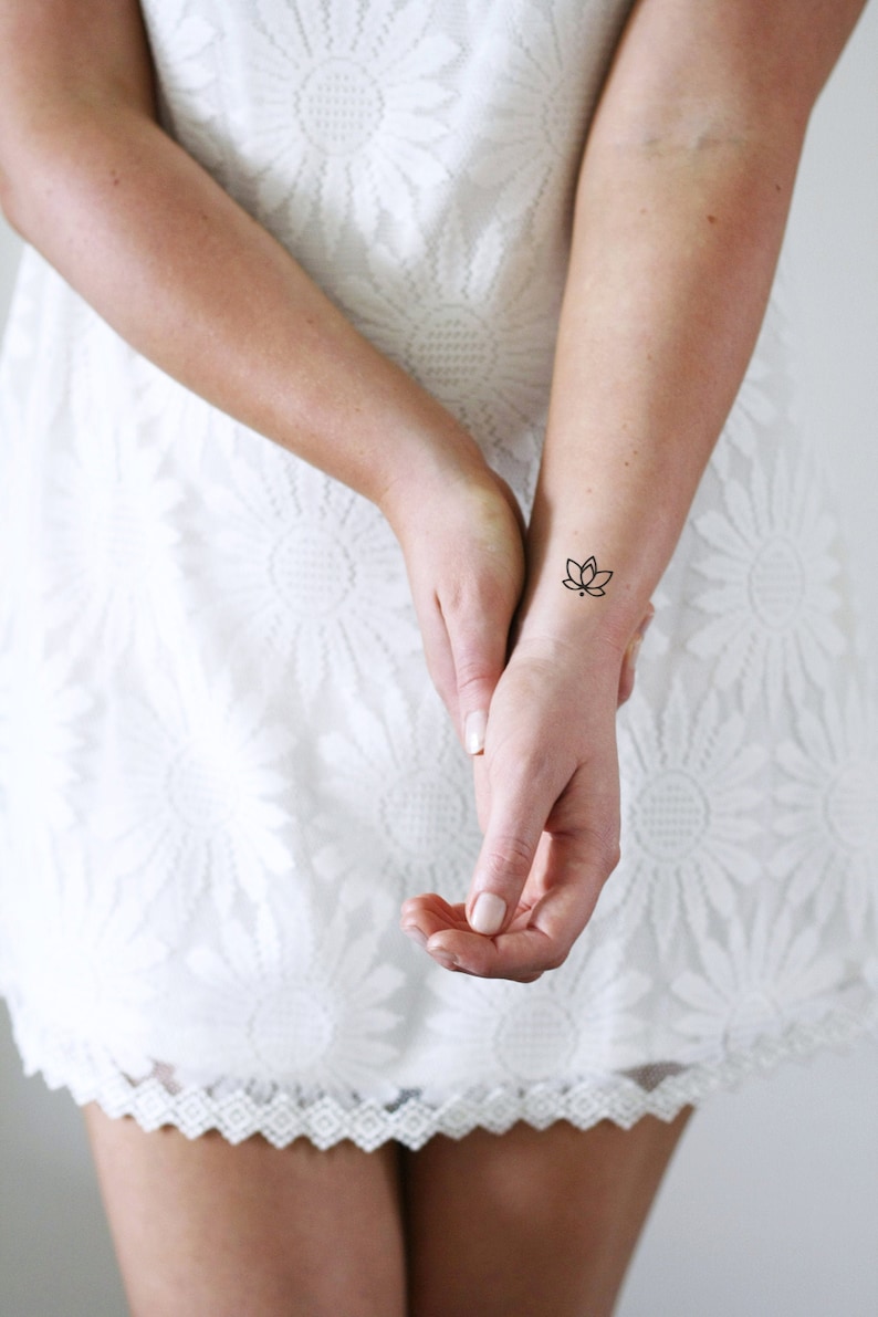 May include: A woman's wrist with a small black lotus flower tattoo.