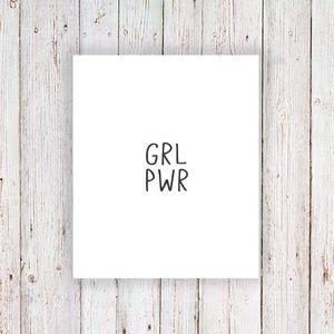 May include: White card with the text "GRL PWR" written in black.