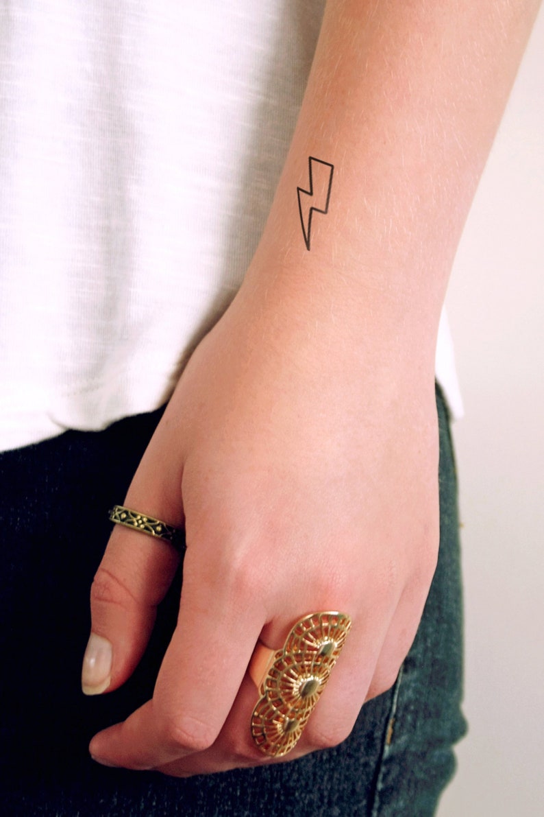 May include: A simple black lightning bolt temporary tattoo on a person's wrist.