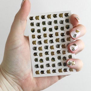 May include: A sheet of nail stickers with a grid of 48 cat faces. The cats are in various colors and patterns, including brown, black, white, and gray.