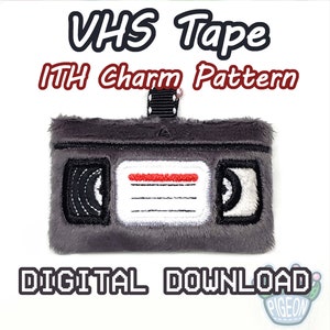 Puede incluir: Un patrón de descarga digital para un amuleto de cinta VHS. El patrón es para un proyecto de bordado en el aro. La imagen muestra una cinta VHS de felpa gris con una etiqueta roja y detalles en blanco y negro.