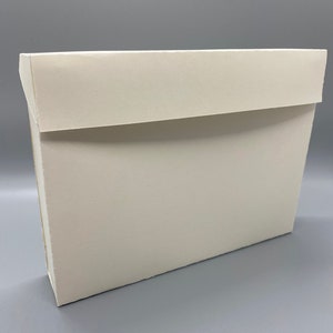 May include: A rectangular white cardboard box with a flat, fold-over lid. The box features a clean, matte finish and a structured design with sharp edges, presenting a simple and functional storage container for various items or documents.